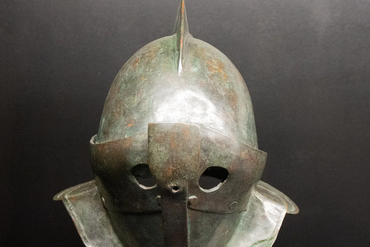 A bronze secutor helmet with a smooth rounded top, a single crest ridge, two small eye holes and flared neck guards