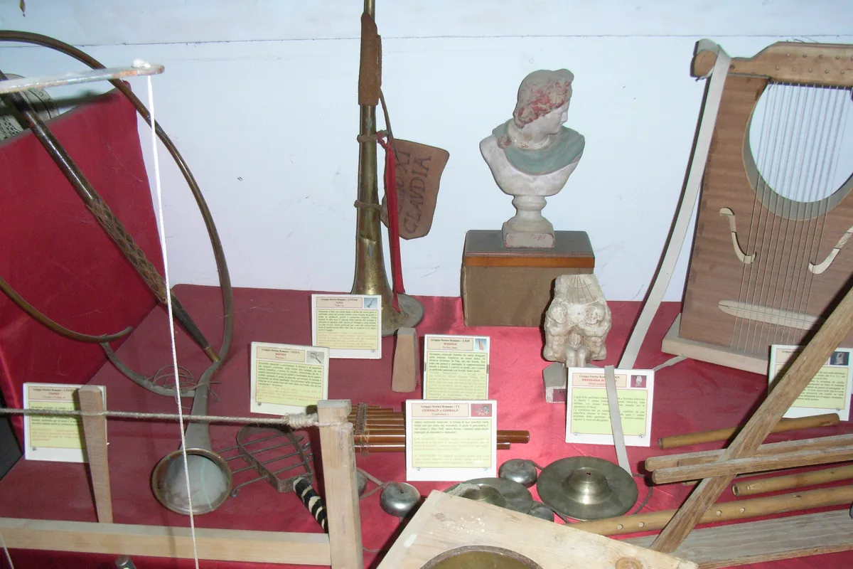 A museum display of reproduction Roman musical instruments, including a bronze horn, a lyre, pan pipes and cymbals, with a plaster bust on a red cloth