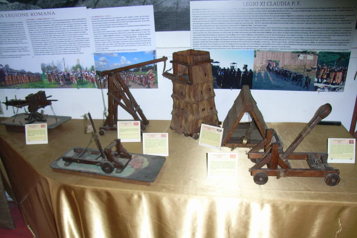 A table of wooden models of Roman siege engines with printed labels, and information panels about the Roman legion on the wall behind